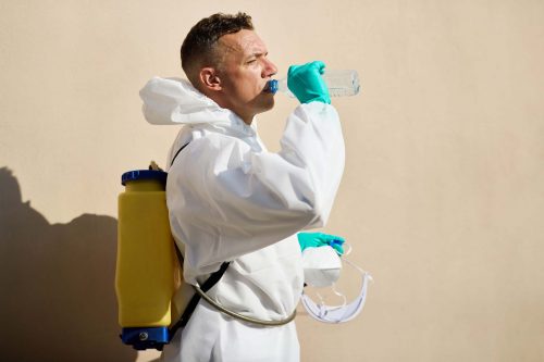 Sanitation worker in hazmat suit having a water break outdoors.